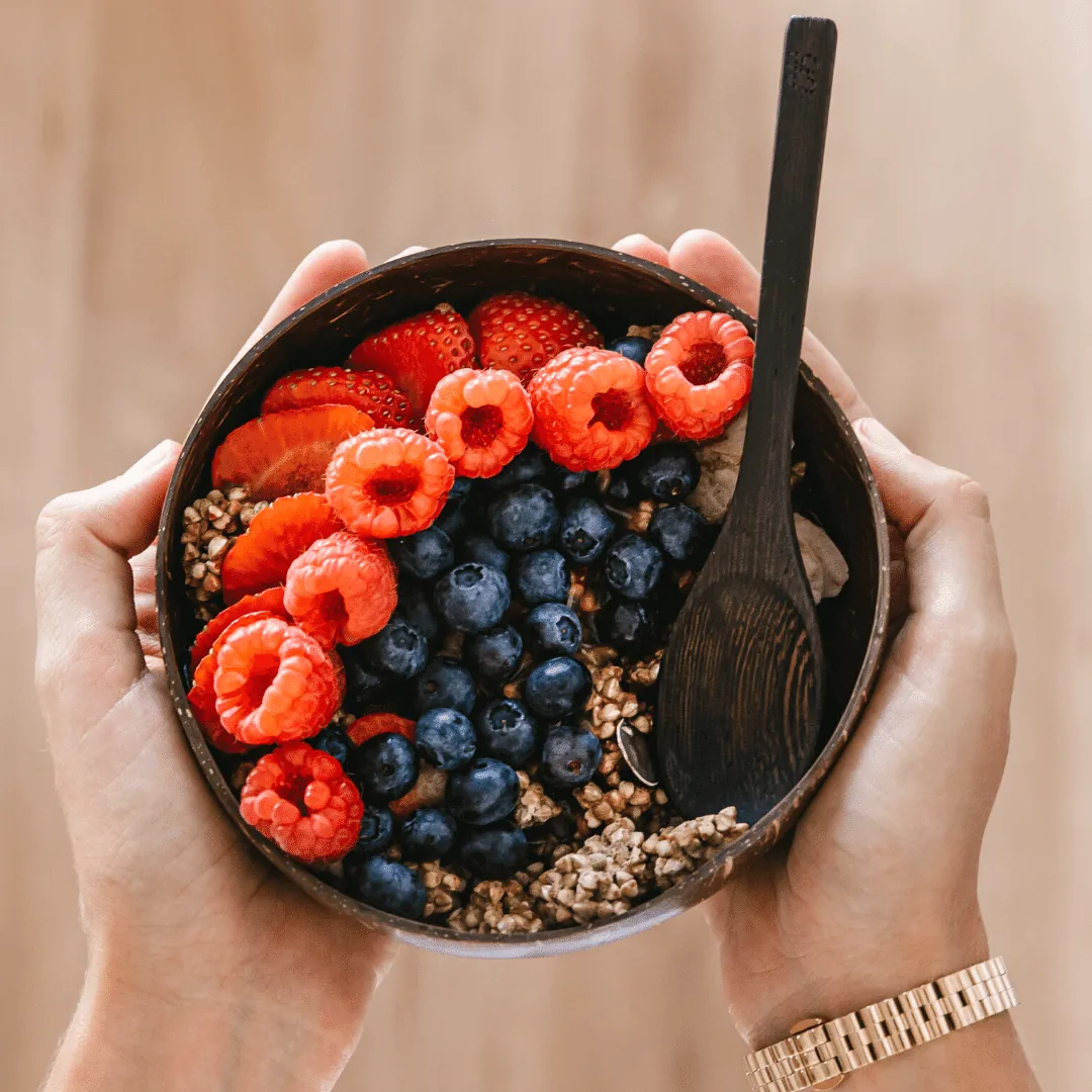 Fresh berries and granola in a coconut bowl held in two hands
