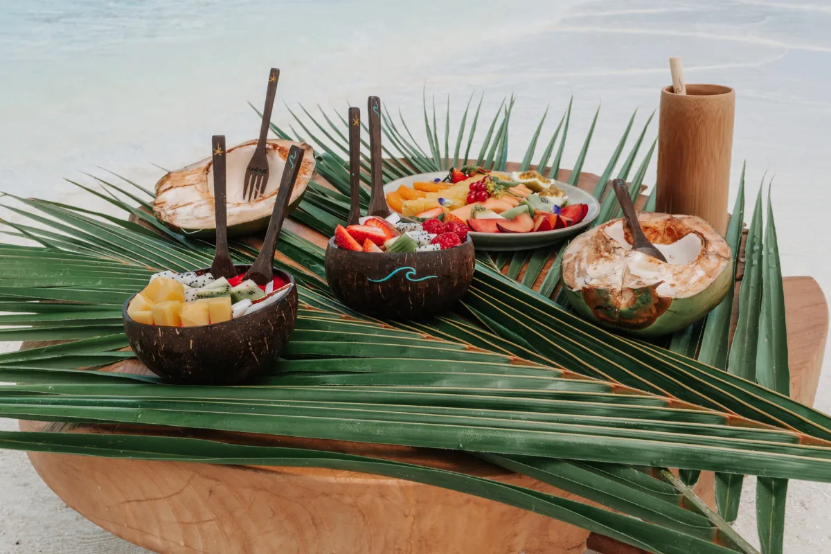 Coconut bowls filled with fresh fruit on palm leaves beside the water