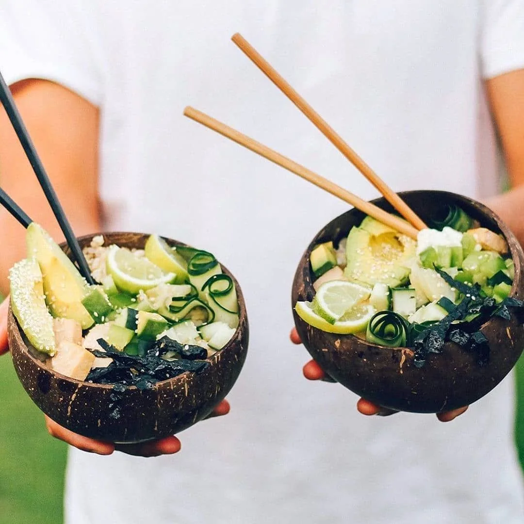 Two people holding coconut bowls filled with fresh food