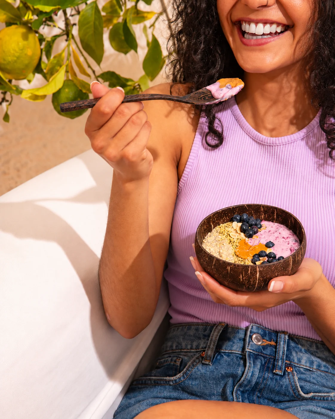 Woman enjoying breakfast from a small coconut bowl with a wooden spoon